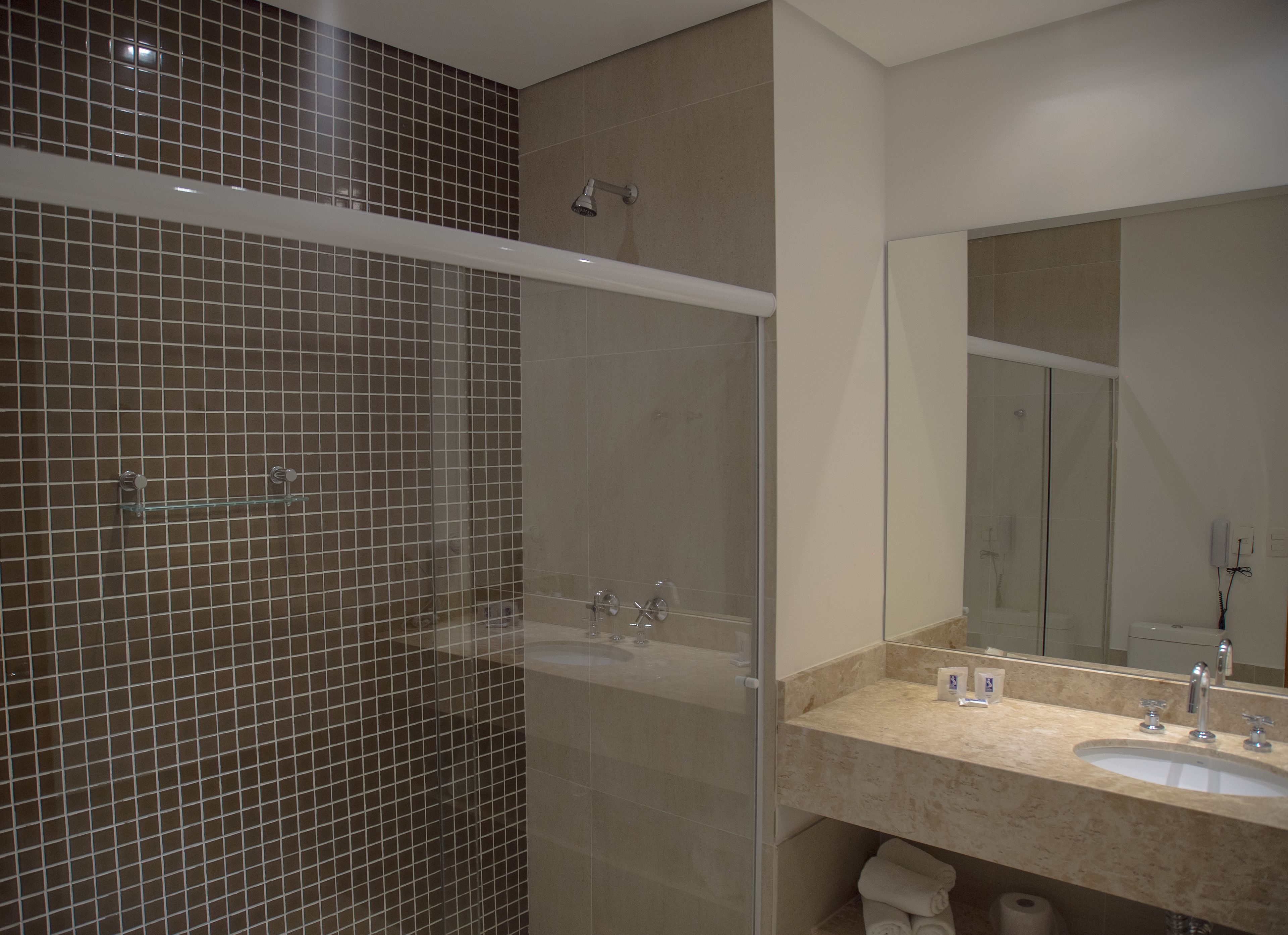 A modern bathroom with a glass-enclosed shower, a large mirror, and a marble countertop.