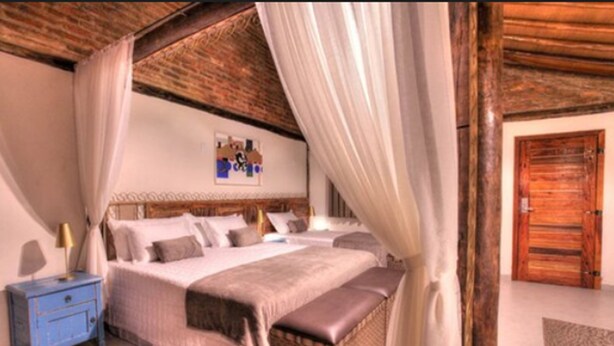 Quarto com uma cama grande, mesa de cabeceira, porta de madeira e um quadro na parede.