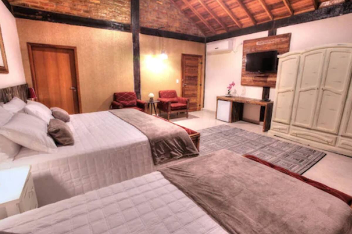 Ein Schlafzimmer mit zwei Betten, einer Holzbalkendecke, einem Fernseher und einem Kleiderschrank.