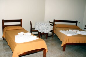 Une chambre d’hôtel avec deux lits simples, une petite table recouverte d’une nappe en dentelle et une chaise.