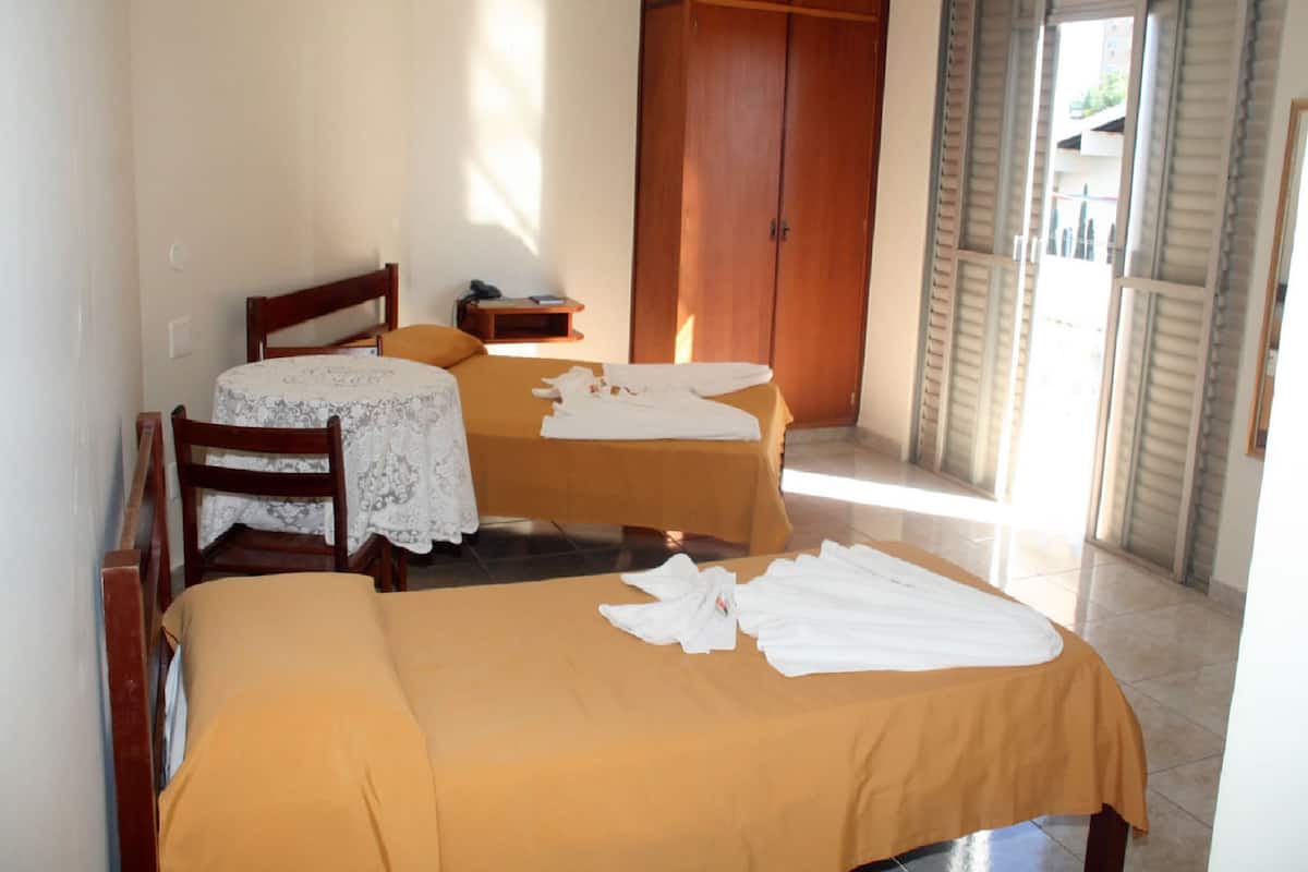 A hotel room with two beds, a wooden wardrobe, a small table, and a chair.