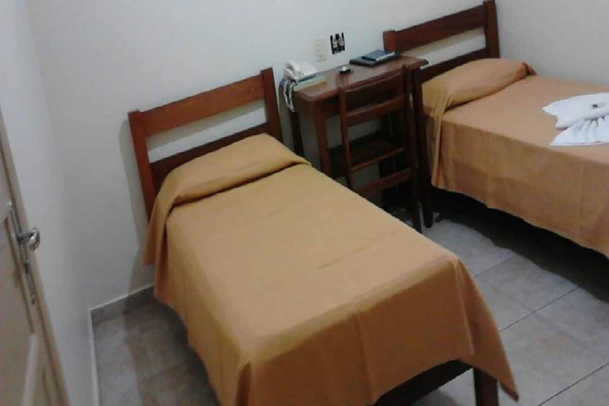 A small, clean room with two single beds, a wooden desk, and a chair.