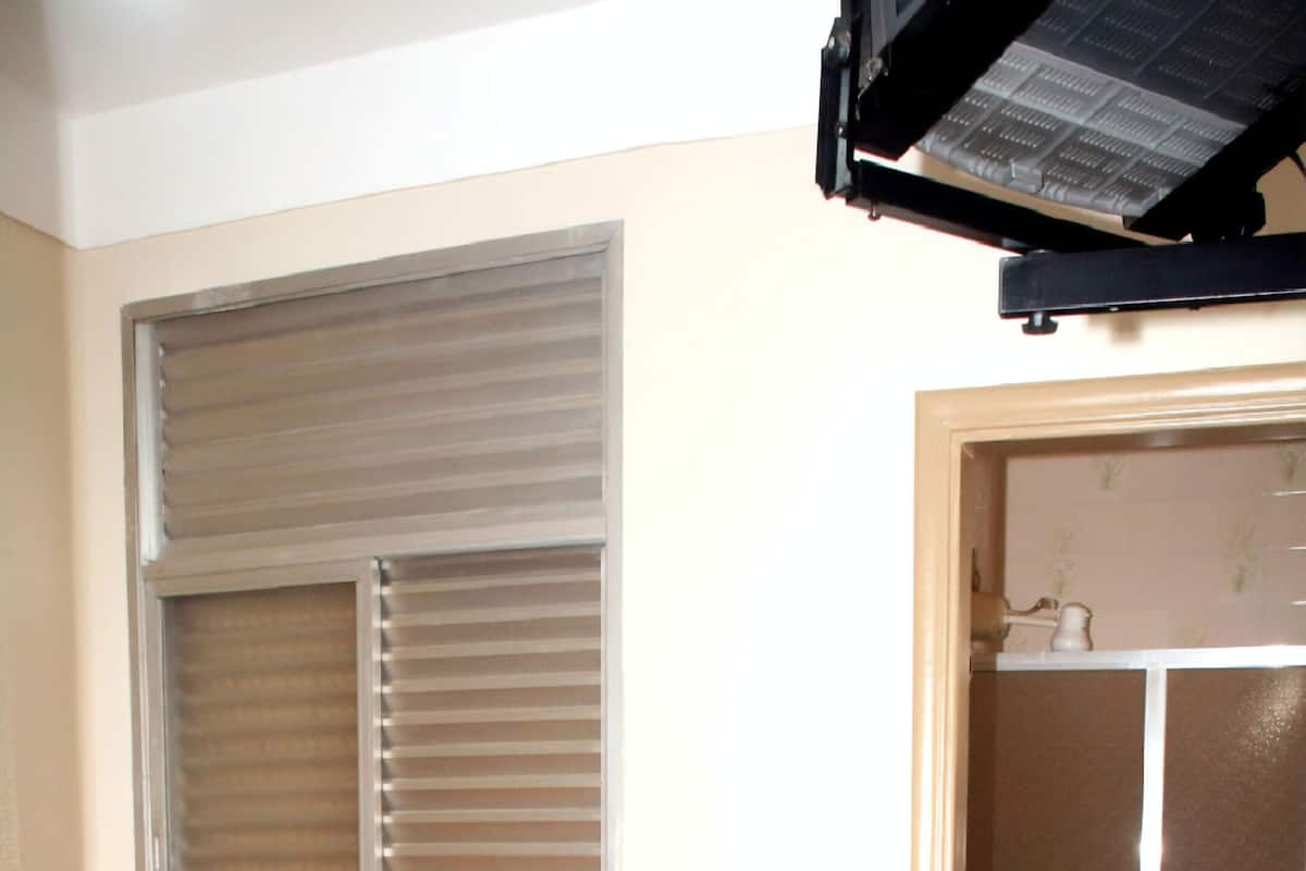 A small room with a bed, a window with blinds, a toilet, and a shower area.