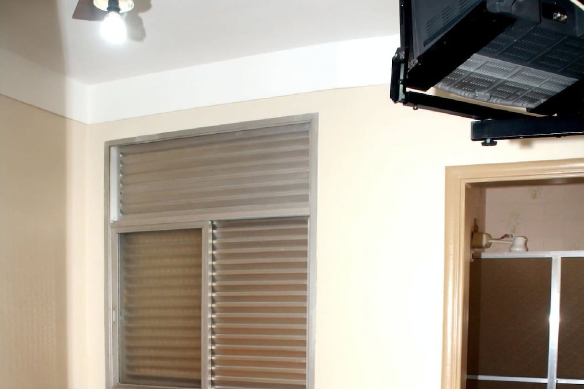 A small room with a bed, a window with blinds, a toilet, and a shower area.