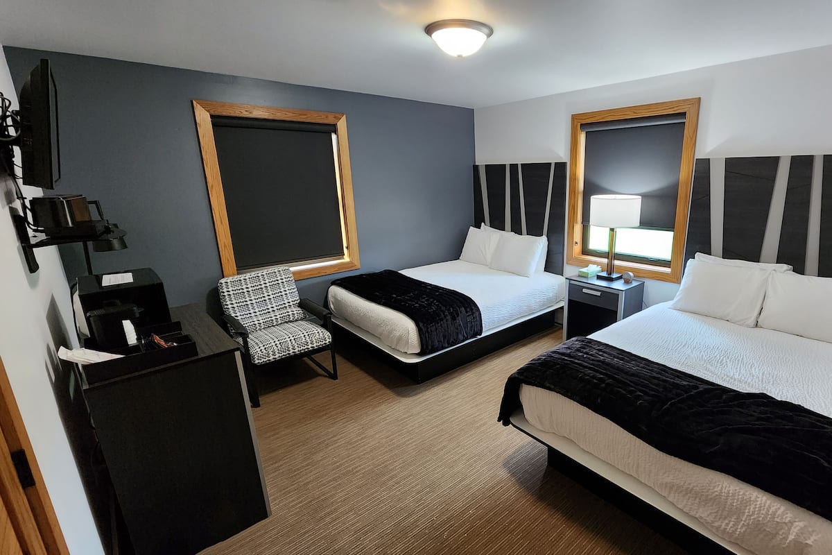 Una habitación de hotel con dos camas, un escritorio, una silla, un televisor y una ventana.