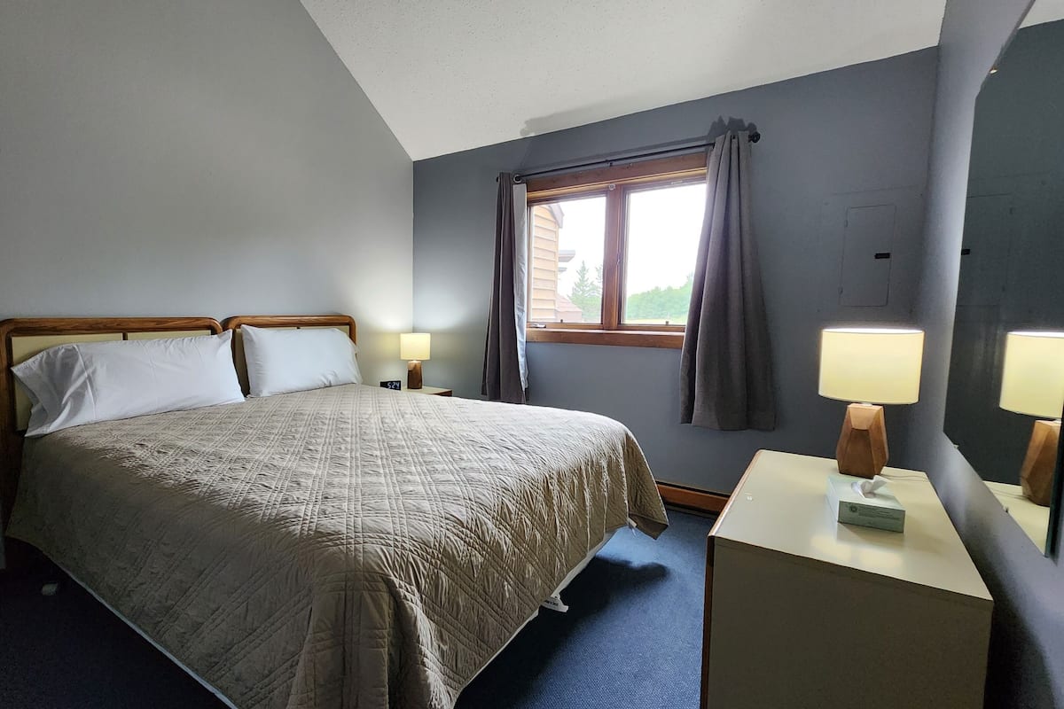 Habitación de hotel ordenada con cama, lámparas de noche, mesita de noche y ventana con cortinas.