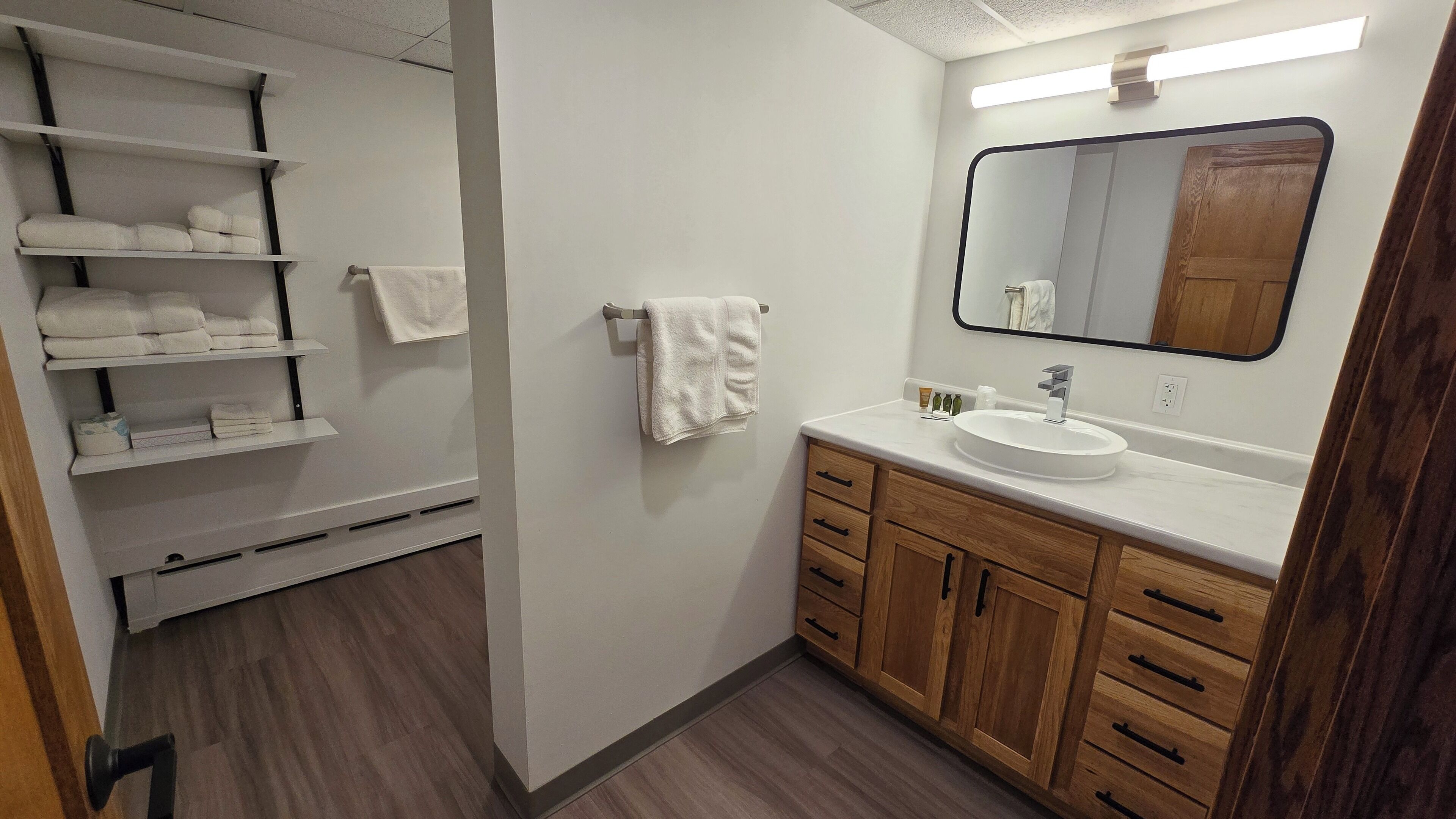 Et moderne badeværelse med et hvidt toiletbord, træskabe og et stort spejl.