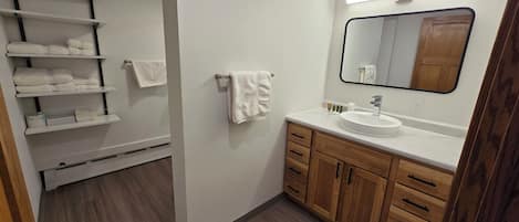 Et moderne badeværelse med et hvidt toiletbord, træskabe og et stort spejl.