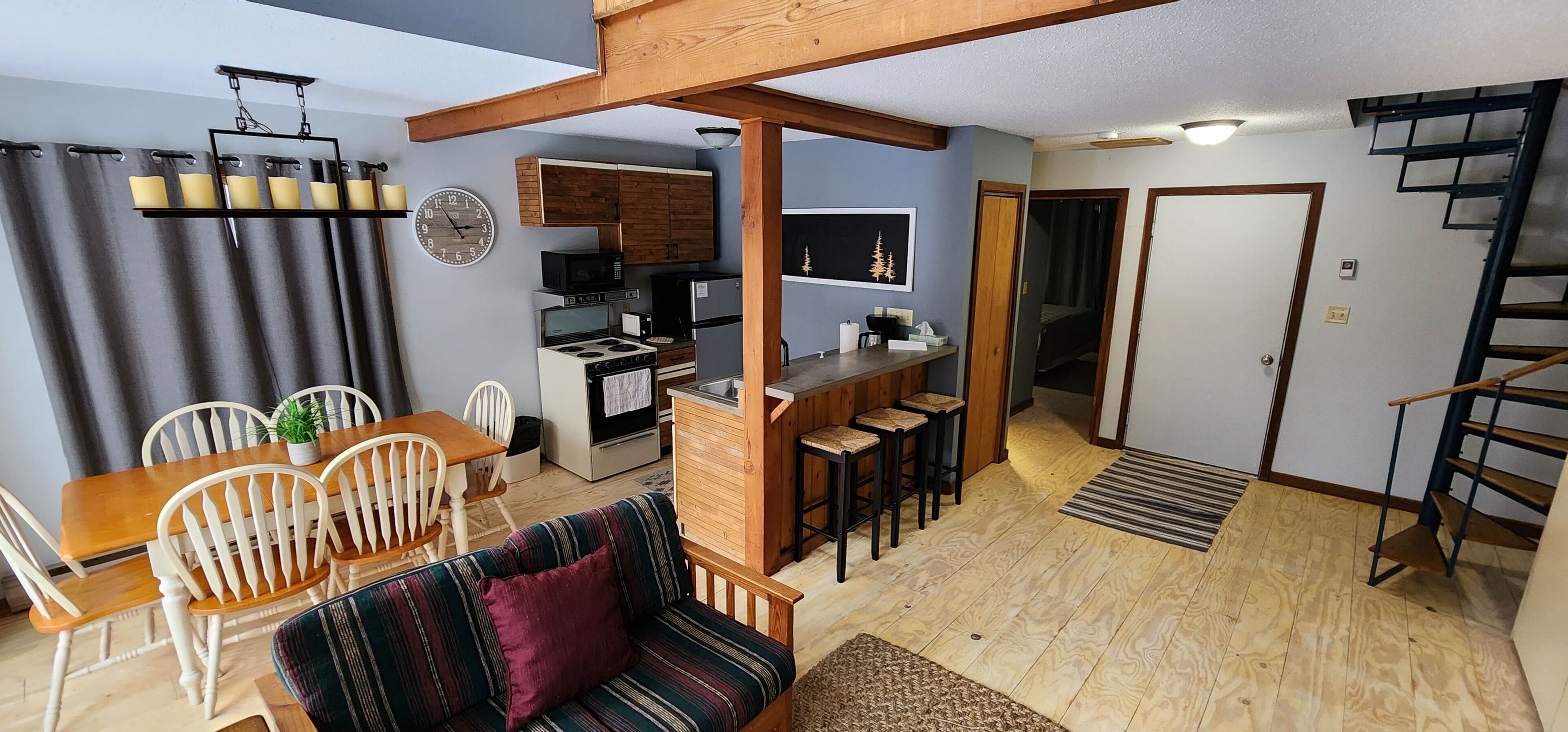 A compact living space with a dining area, a sofa, a kitchen, and a staircase.