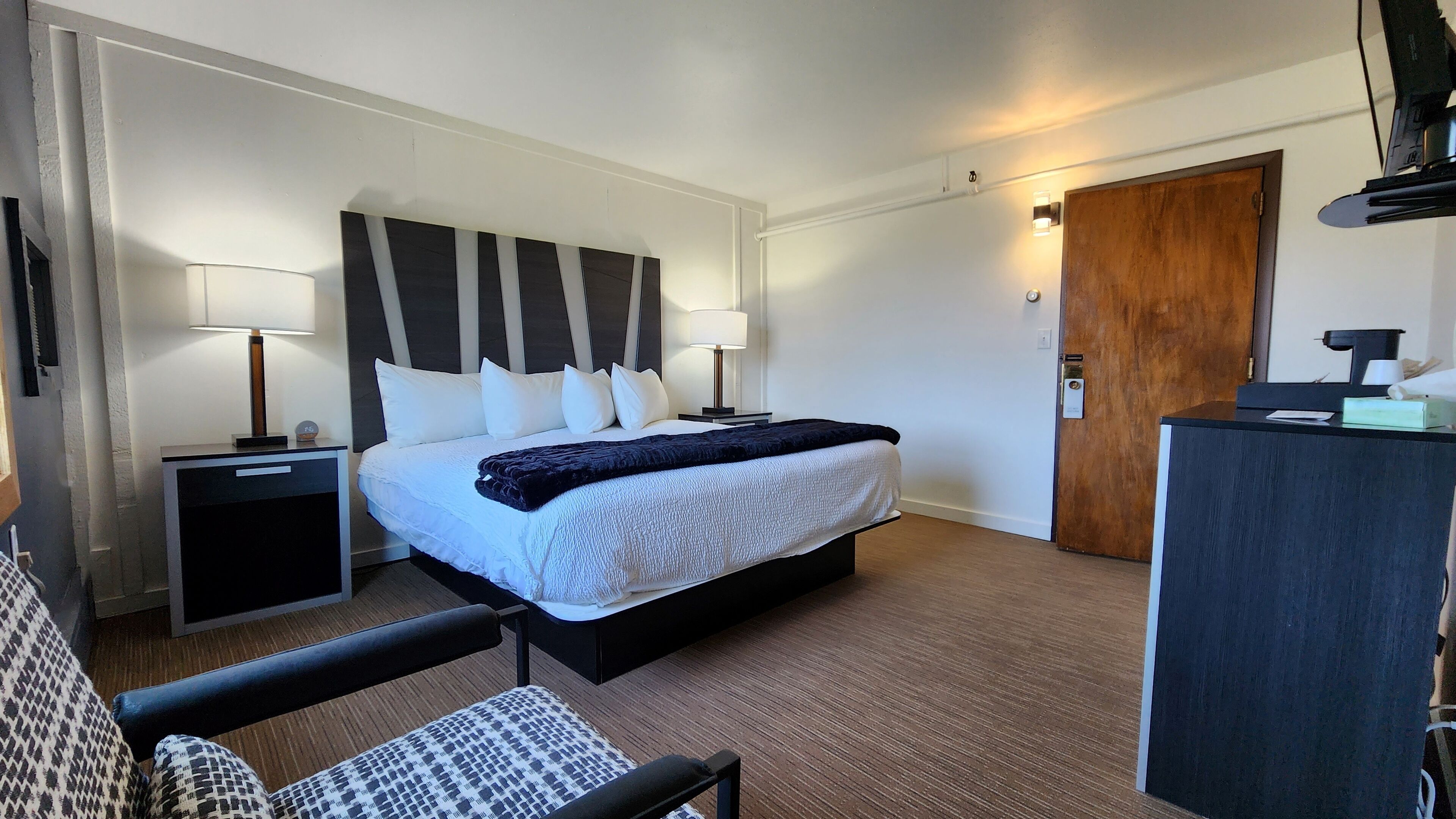 Una habitación de hotel con una cama grande, lámparas de noche, un escritorio y una silla.