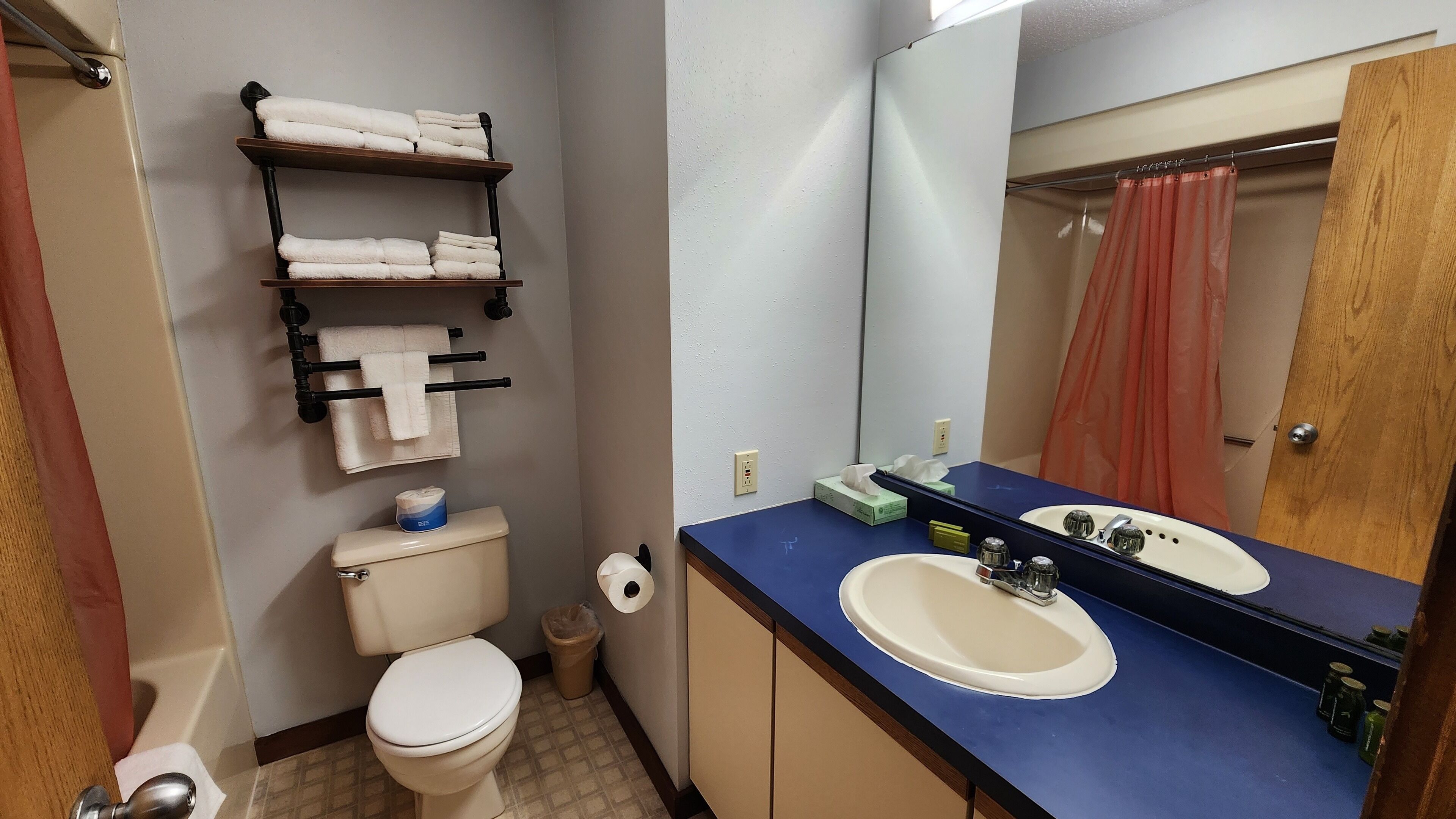 Une salle de bain équipée de toilettes, d’un lavabo et d’étagères où sont rangées les serviettes.