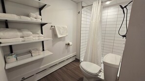 A modern bathroom with a toilet, shower, and shelves with towels. - Snowriver Mountain Resort (Wakefield)