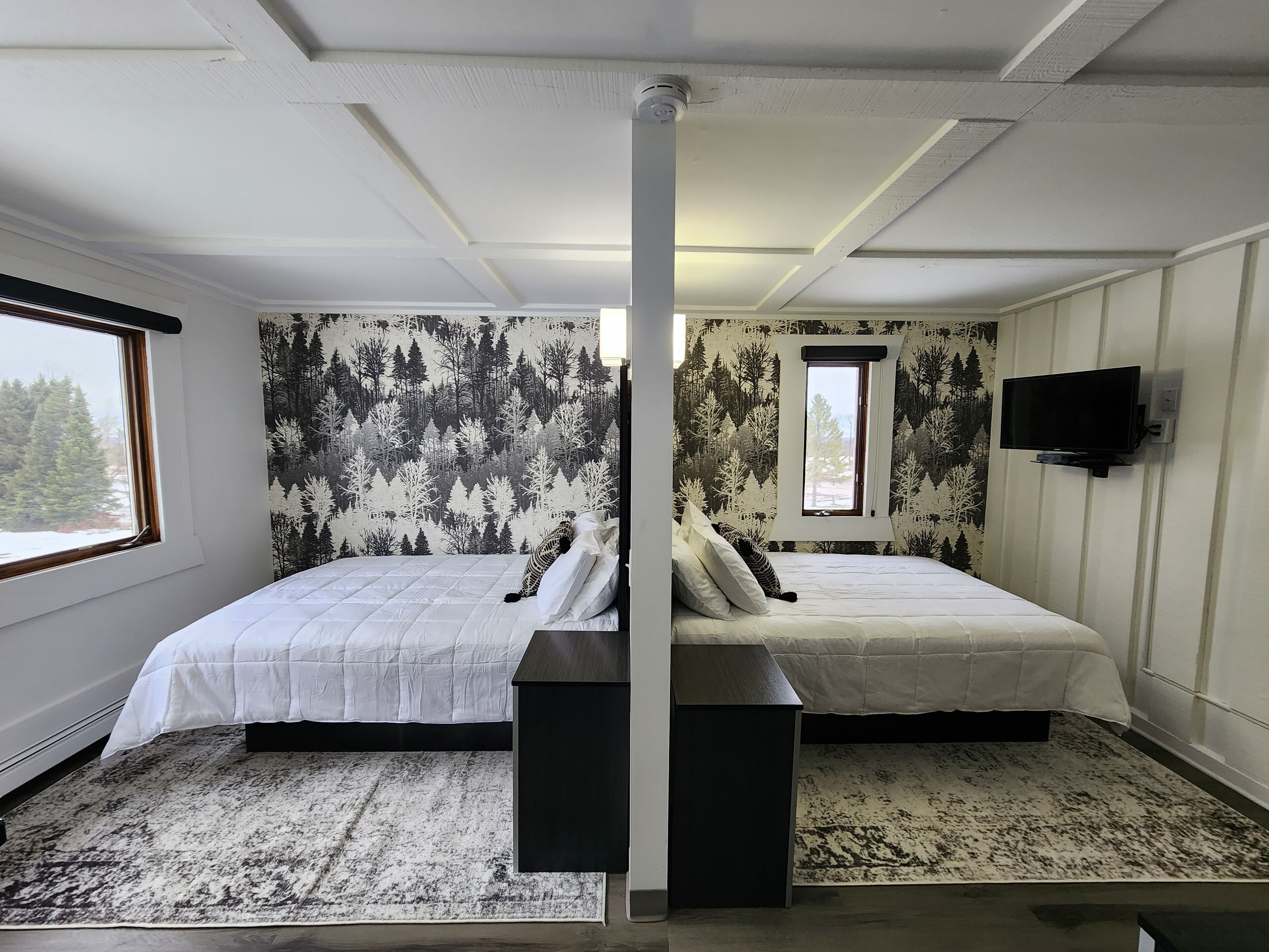 A room with two beds, a large window, a television, and a patterned wall.