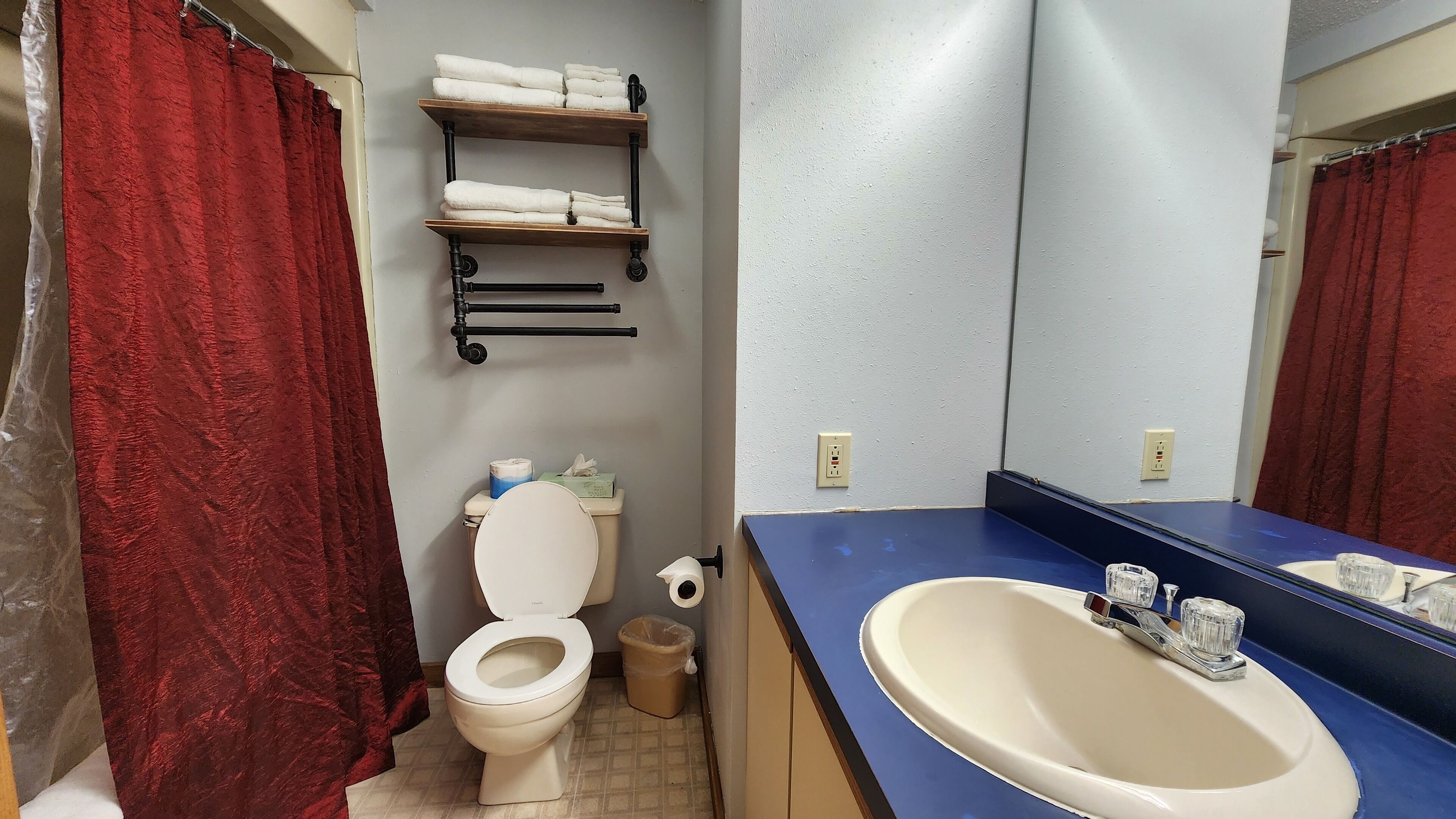 A bathroom with a toilet, a sink, a mirror, and shelves with towels.