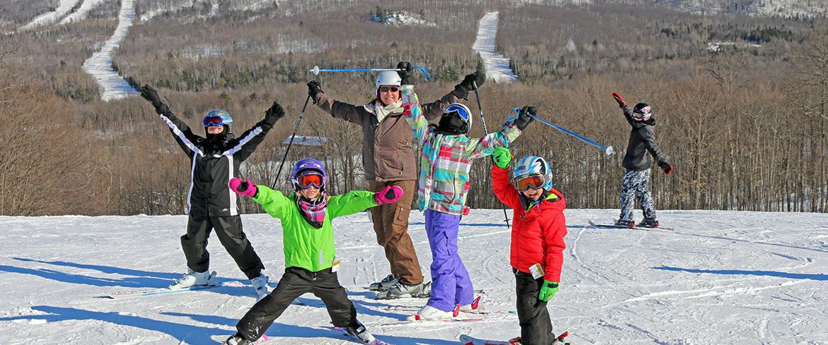 A group of people skiing on a snowy slope with a clear sky and trees in the background.