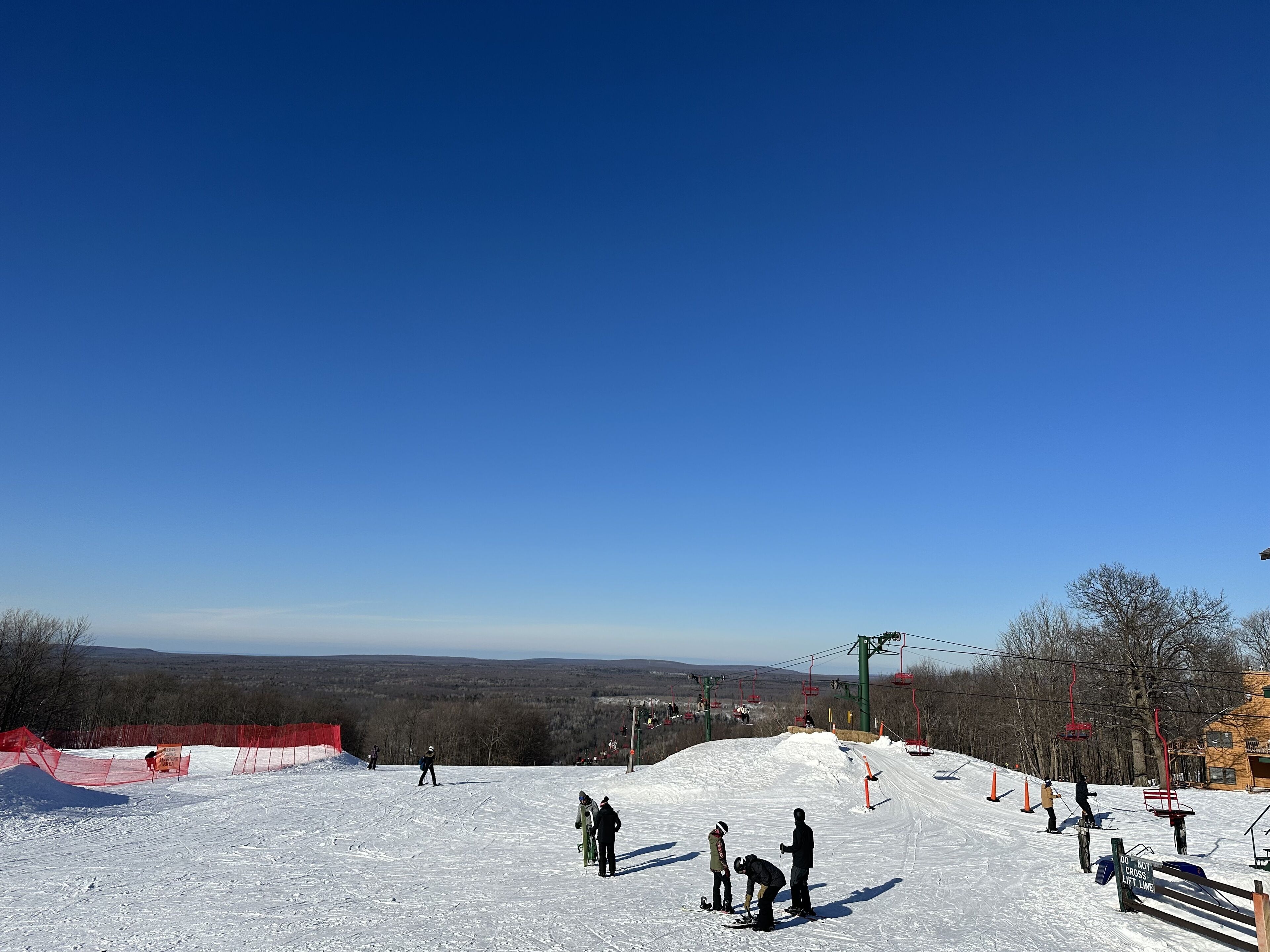 Pista de esquí con cielo azul despejado, un telesilla y vista distante de un pueblo.