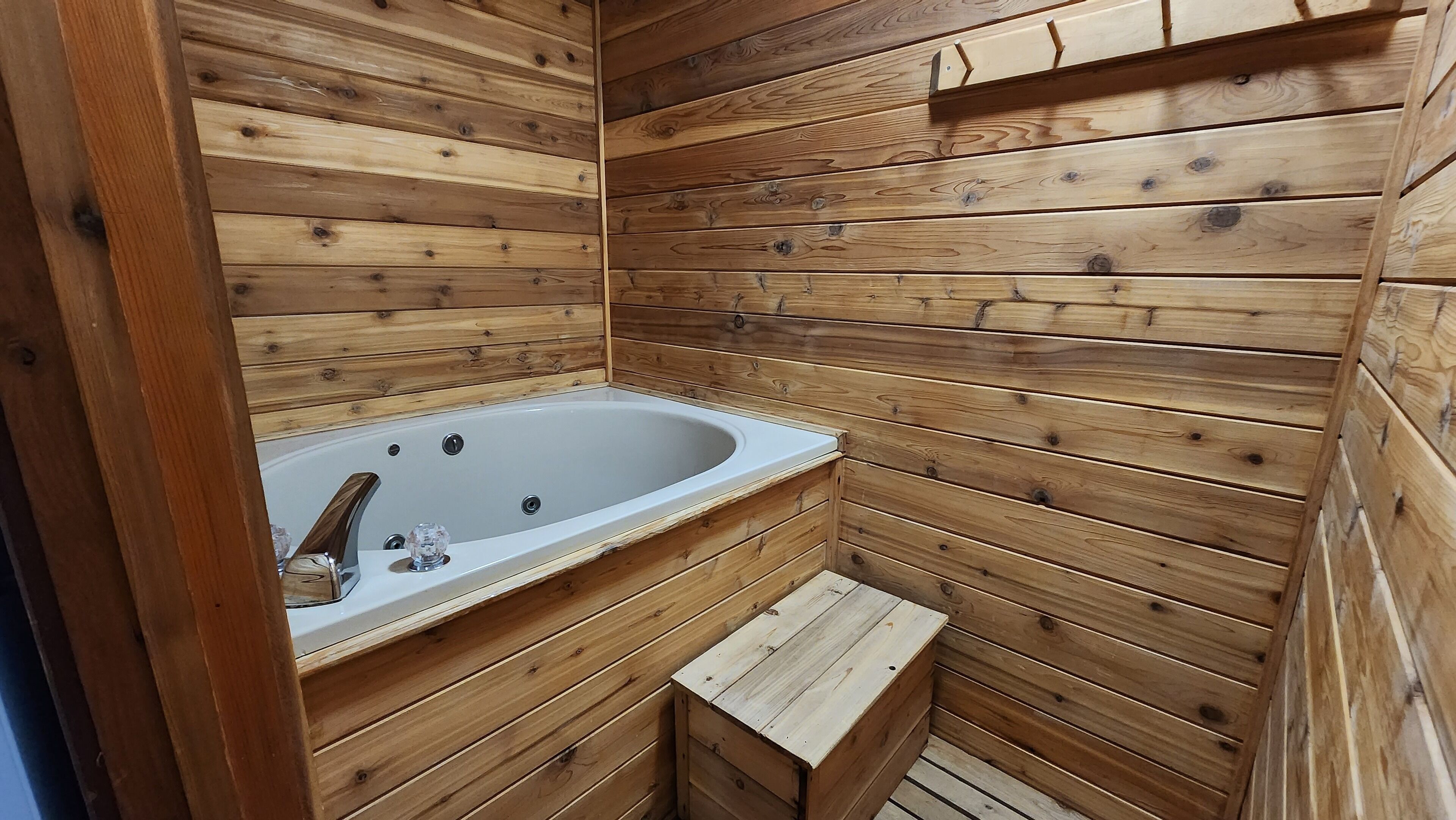 Una cabaña de madera con bañera incorporada y un pequeño banco de madera.