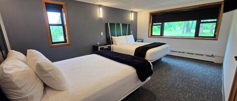 A hotel room with two beds, a large window with a view of greenery, and a ceiling light.