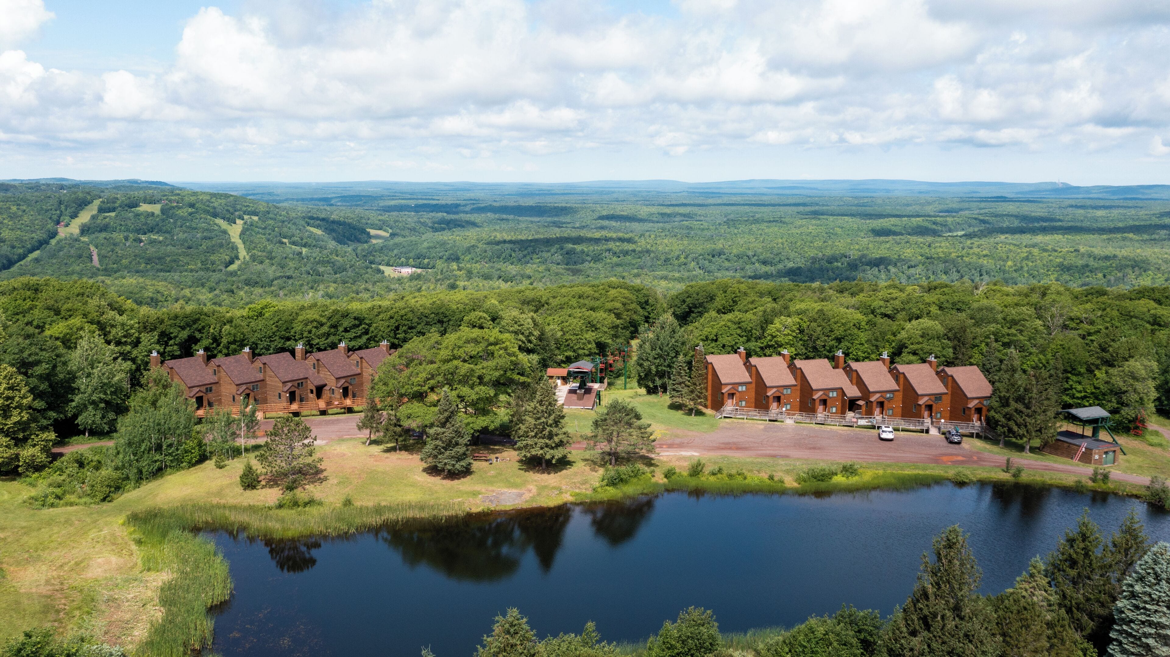 Eine Lodge mit mehreren Backsteingebäuden, einem Teich und einer bewaldeten Landschaft im Hintergrund.