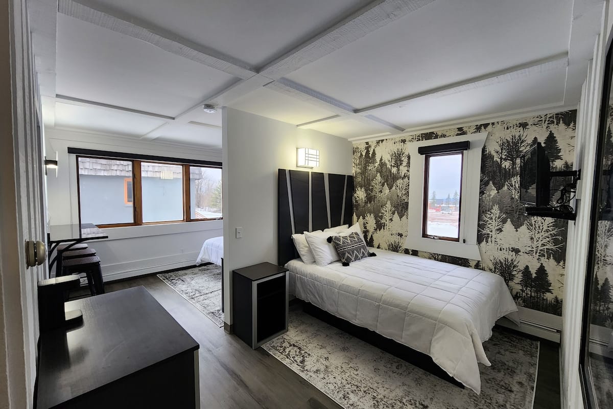 Un dormitorio moderno con una cama grande, un escritorio y vistas a un paisaje nevado a través de la ventana.