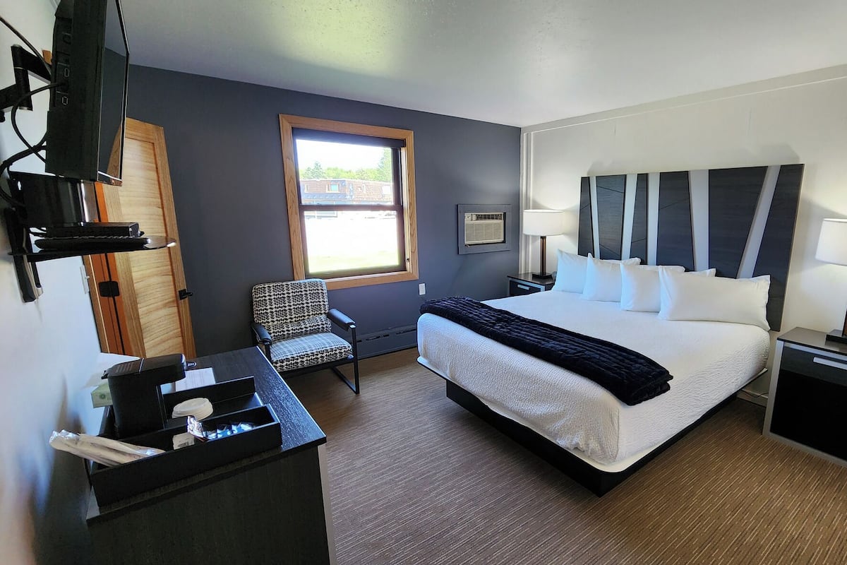 Habitación de hotel con cama, mesitas de noche, escritorio con silla, televisor y ventana con vistas a edificios.