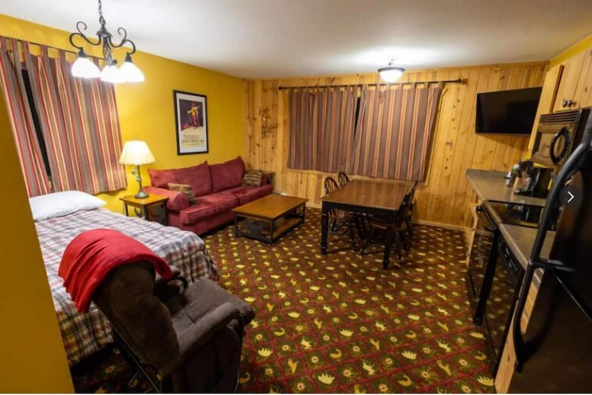 Una habitación funcional con cama, sofá, mesa de comedor y zona de cocina.