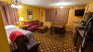 A compact room with a bed, a sofa, a dining table, and a kitchen area.