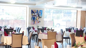 A restaurant with multiple tables set for dining, featuring a large window view and a colorful abstract painting on the wall. - Tomreik Hotel (Accra)