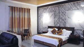 A hotel room with a large bed, a wooden headboard, two bedside tables, a nightstand, and a seating area with a chair and a sofa. - Tomreik Hotel (Accra)