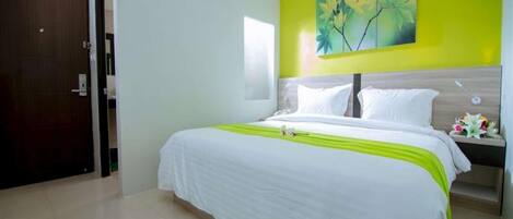A hotel room with a bed, a nightstand, a painting on the wall, and a pair of slippers on the floor.