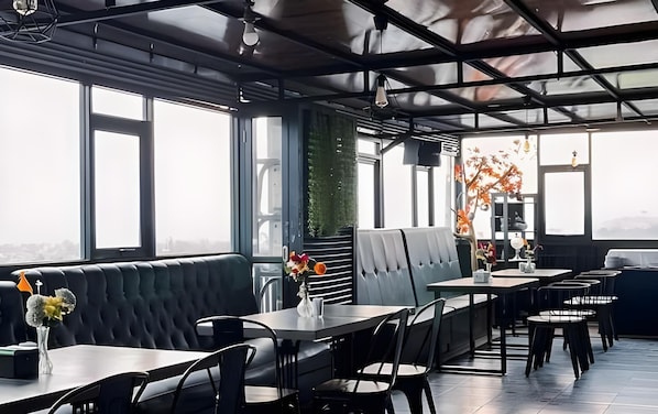 A modern restaurant with a high ceiling, large windows, and a mix of seating including booths and tables.
