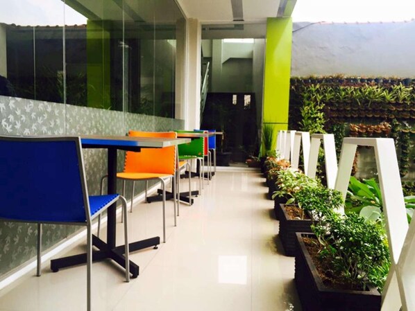 A waiting area with chairs and tables, a glass wall, and potted plants. - Fresh Hotel Sukabumi (Sukabumi)