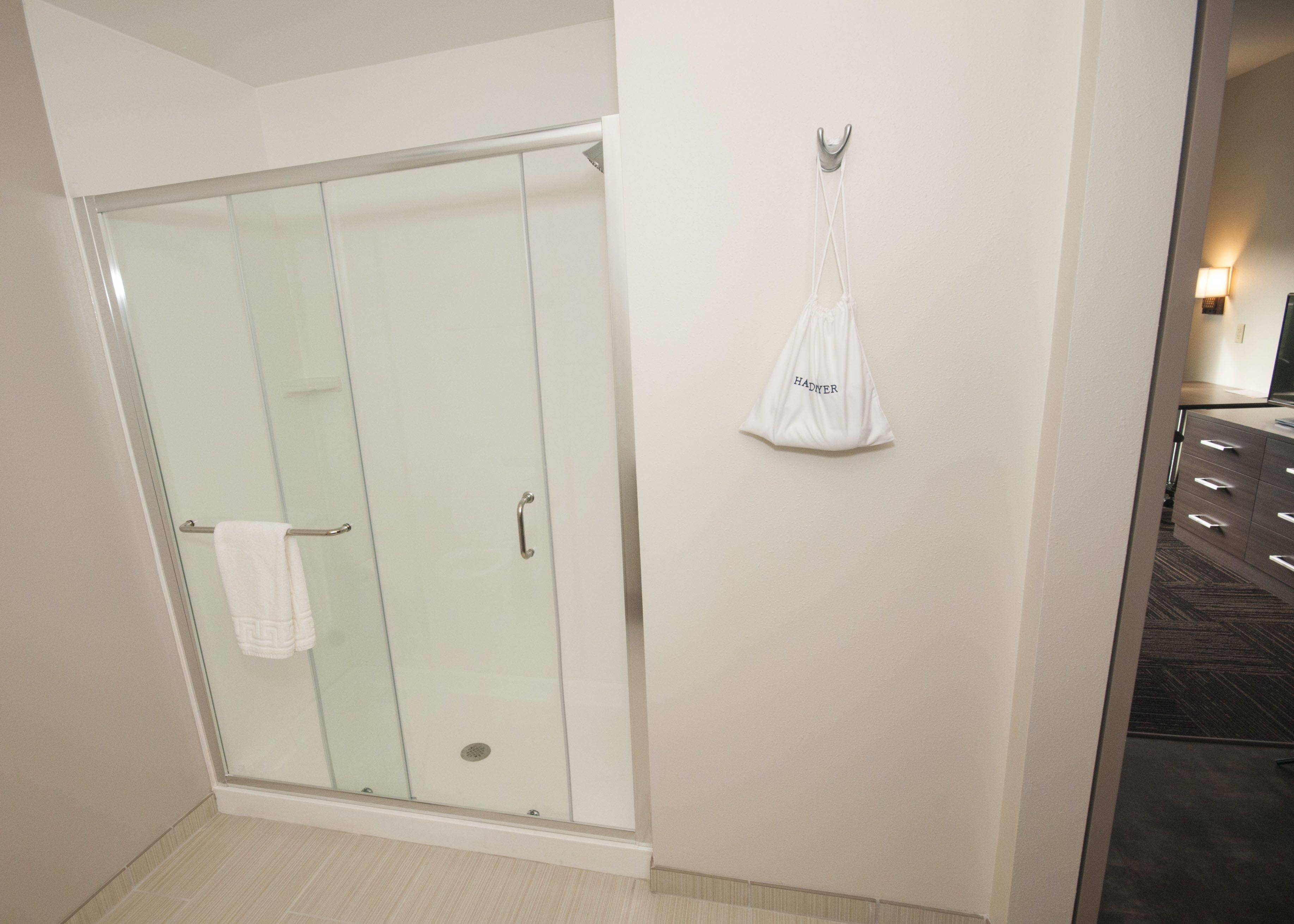 A modern bathroom with a glass shower enclosure, a white towel hanging on the door, and a white bag hanging on the wall.