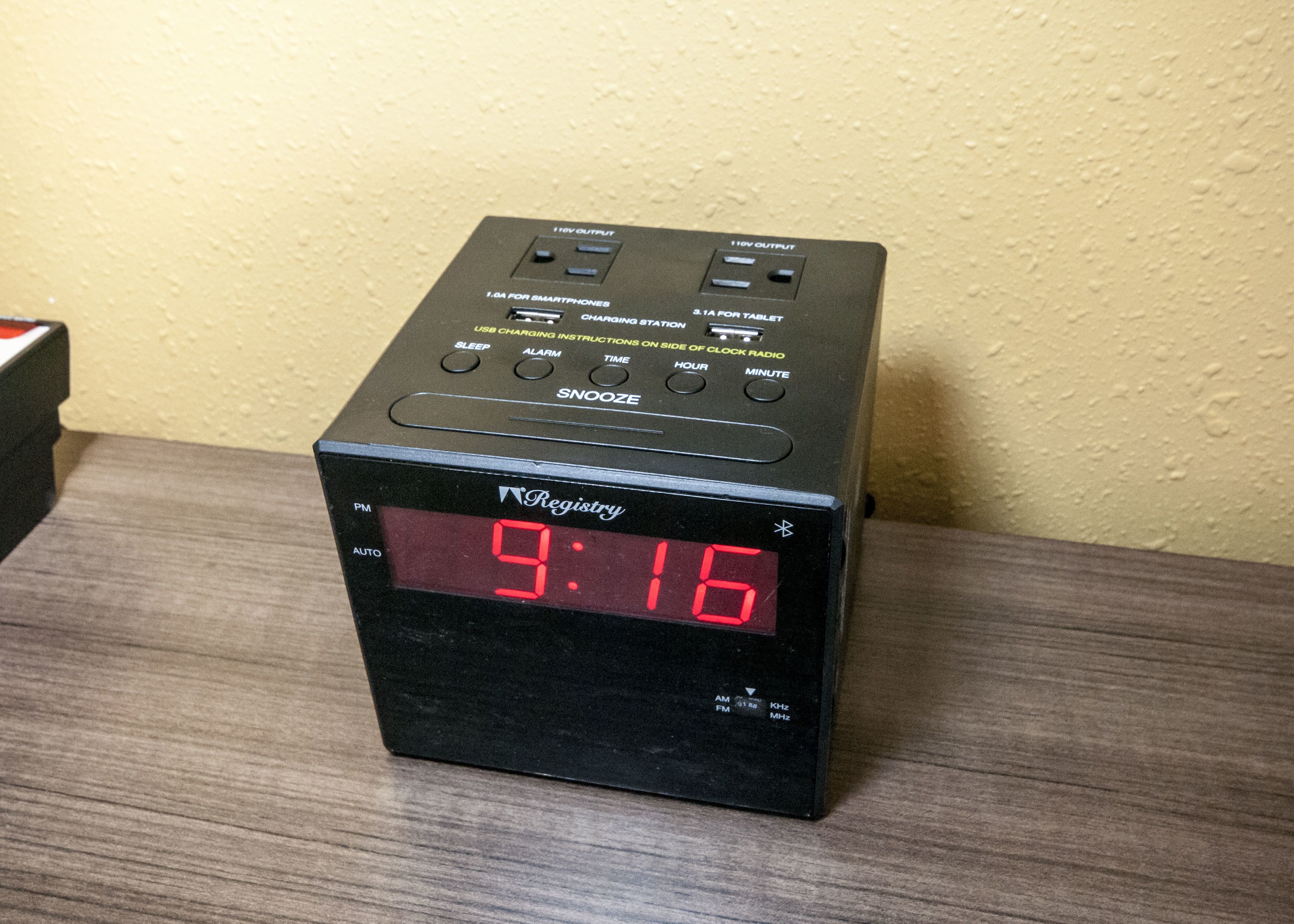 A black digital clock with red LED display on a wooden surface.