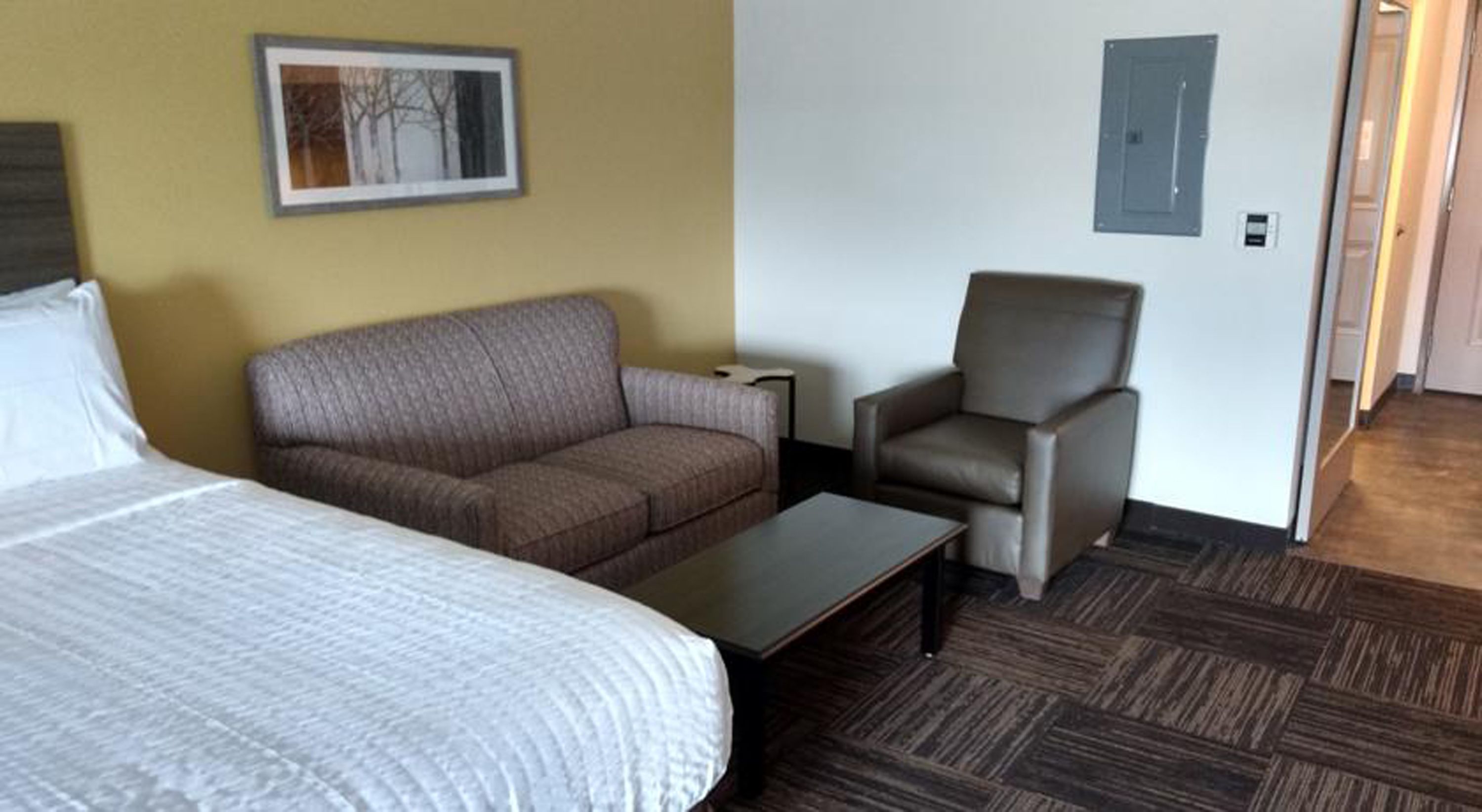 A hotel room with a bed, a sofa, a chair, and a small table.