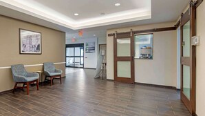 A hotel lobby with a wooden floor, two grey armchairs, a framed picture on the wall, and a sliding glass door. - Extended Stay America Suites Rock Hill (Rock Hill)