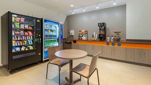 A small, modern cafe with a round table and chairs, a coffee machine, and vending machines. - Extended Stay America Suites Rock Hill (Rock Hill)