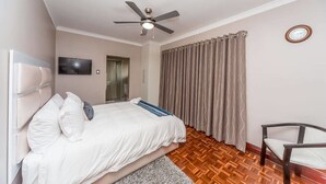 A bedroom with a bed, a ceiling fan, a TV, a chair, and a window with curtains. - The Musafer Travel Lodge (Pietermaritzburg)