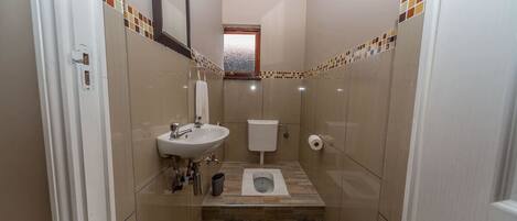 A compact bathroom with a sink, toilet, and steps leading to a window.