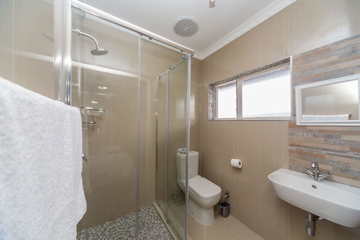 Une salle de bain moderne dotée d’une douche à parois de verre, de toilettes et d’un lavabo agrémenté d’un pare-éclaboussures décoratif.
