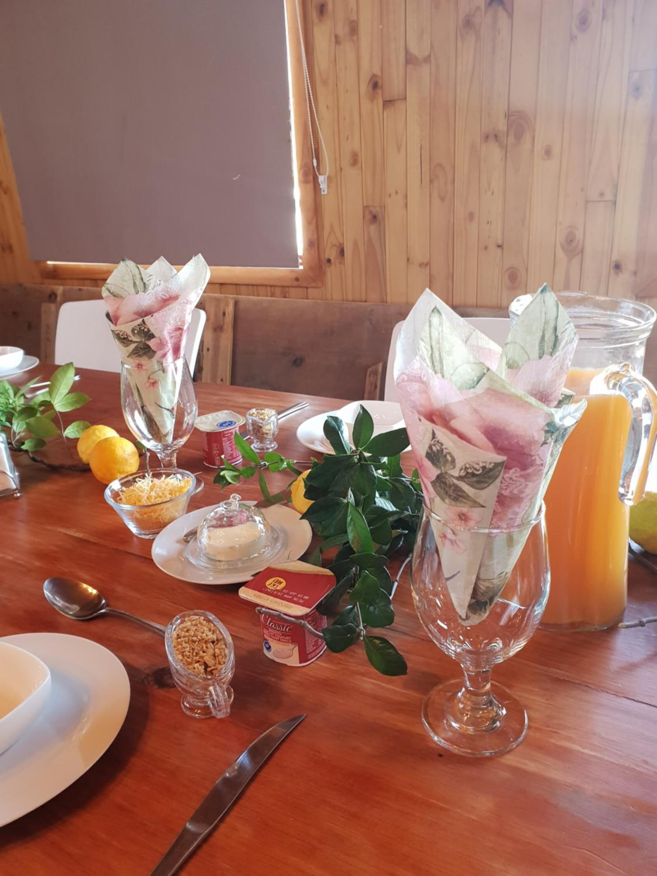 A wooden dining table with a white plate, a glass of juice, and a vase with a floral design.