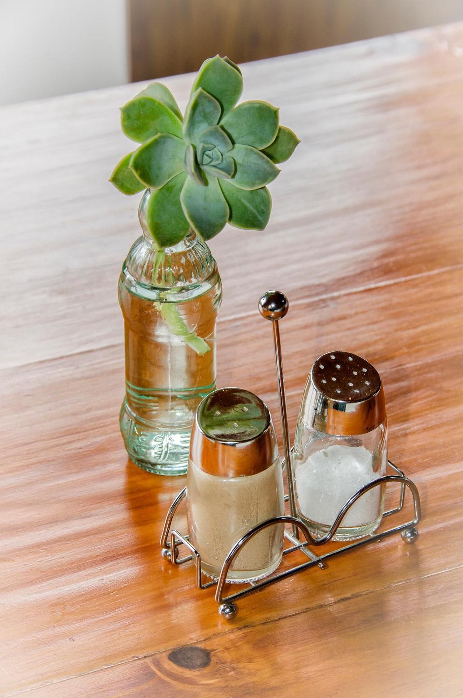 Una mesa de madera con una botella de vidrio, un salero de metal y un pimentero de metal.