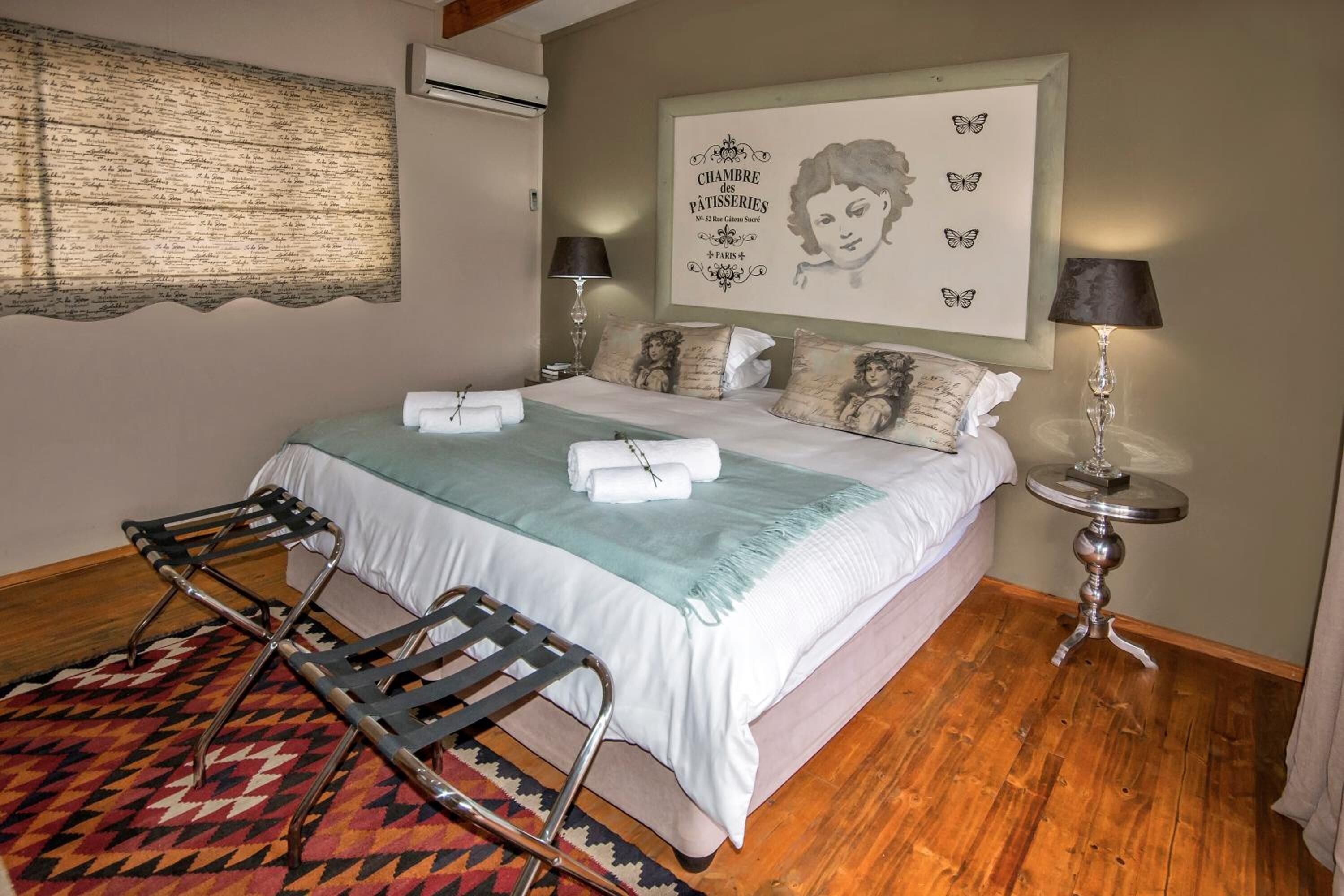 Un dormitorio con cama, almohadas, una mesita de noche, lámpara, un cuadro en la pared y una alfombra estampada.