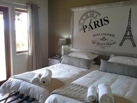 A hotel room with two beds, a large wall clock, and a view of the Eiffel Tower.