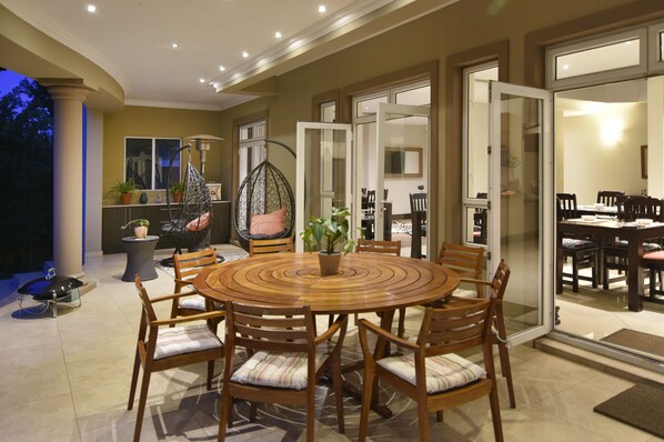 A dining area with a round wooden table and chairs, surrounded by glass doors leading to another room.