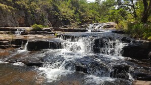 A natural waterfall cascading over rocky terrain surrounded by lush greenery.