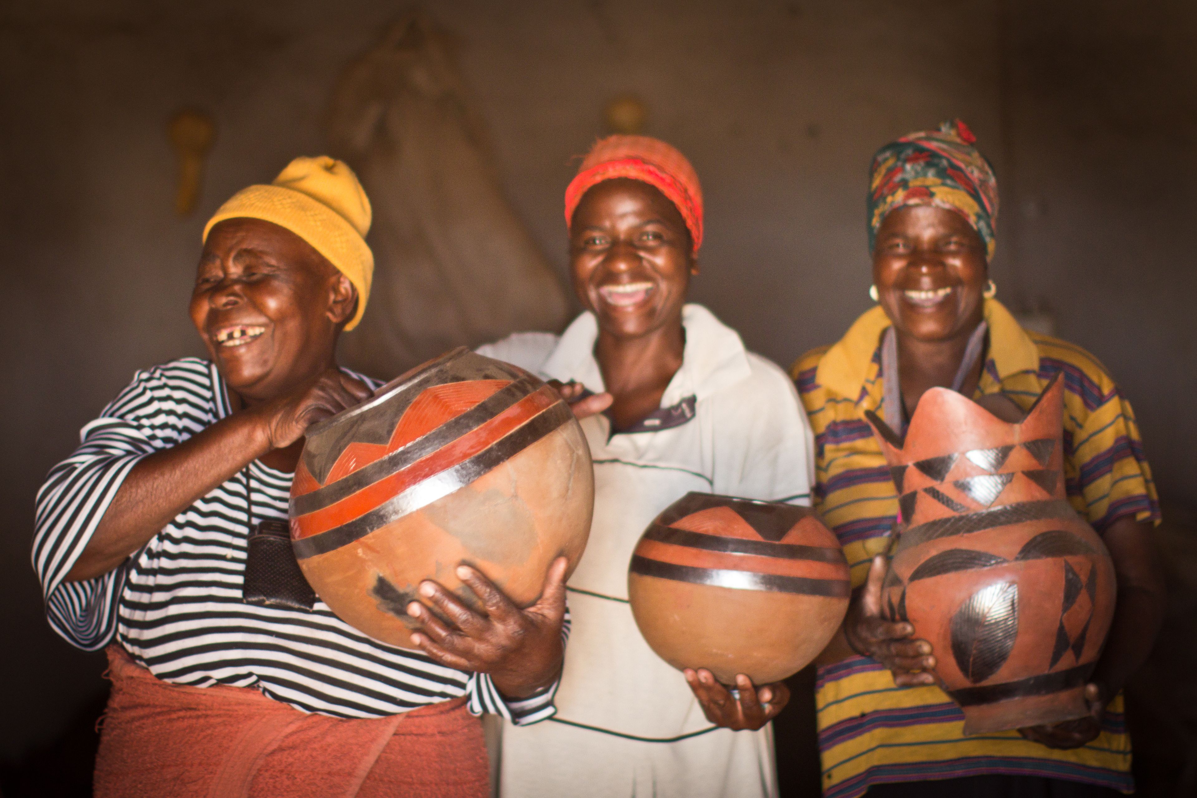 Three people holding large pottery items.