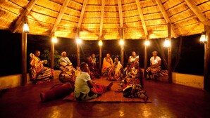 A group of people seated under a thatched roof structure with wooden beams and hanging light fixtures.