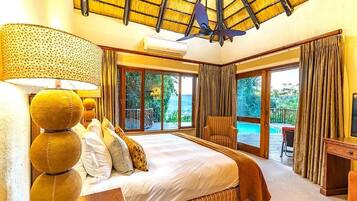 Une chambre d’hôtel avec un grand lit, un coin salon donnant sur la piscine et un balcon avec des rideaux.