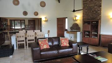 Un salon avec un canapé en cuir marron, une table basse et un coin repas comprenant des chaises en bois et un mur en briques.